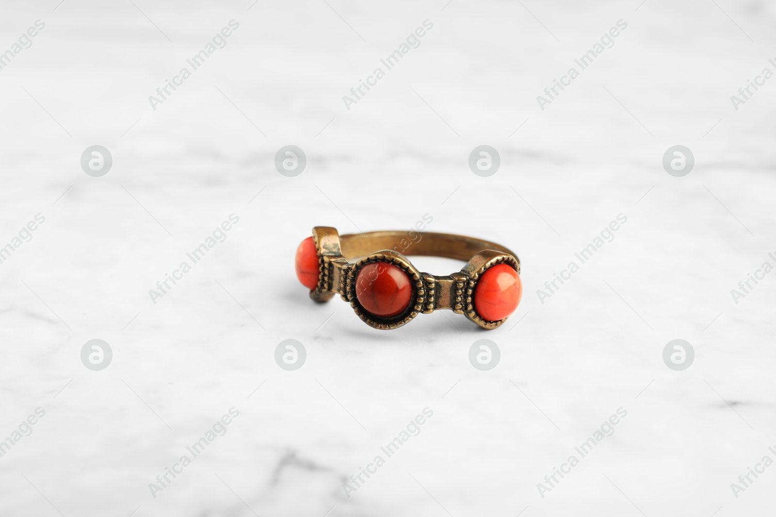 Photo of Beautiful bijouterie. Stylish ring on white marble table, closeup