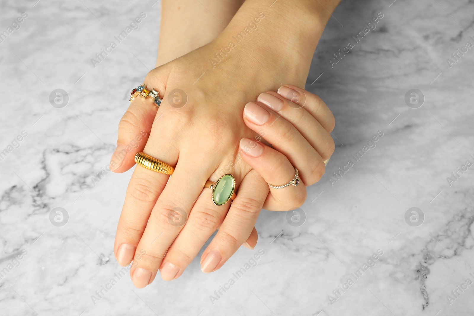 Photo of Beautiful bijouterie. Woman wearing different stylish rings at white marble table, closeup