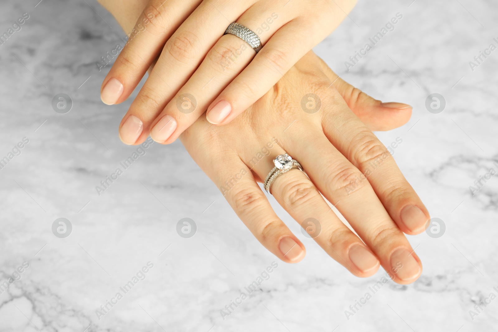 Photo of Beautiful bijouterie. Woman wearing different stylish rings at white marble table, closeup