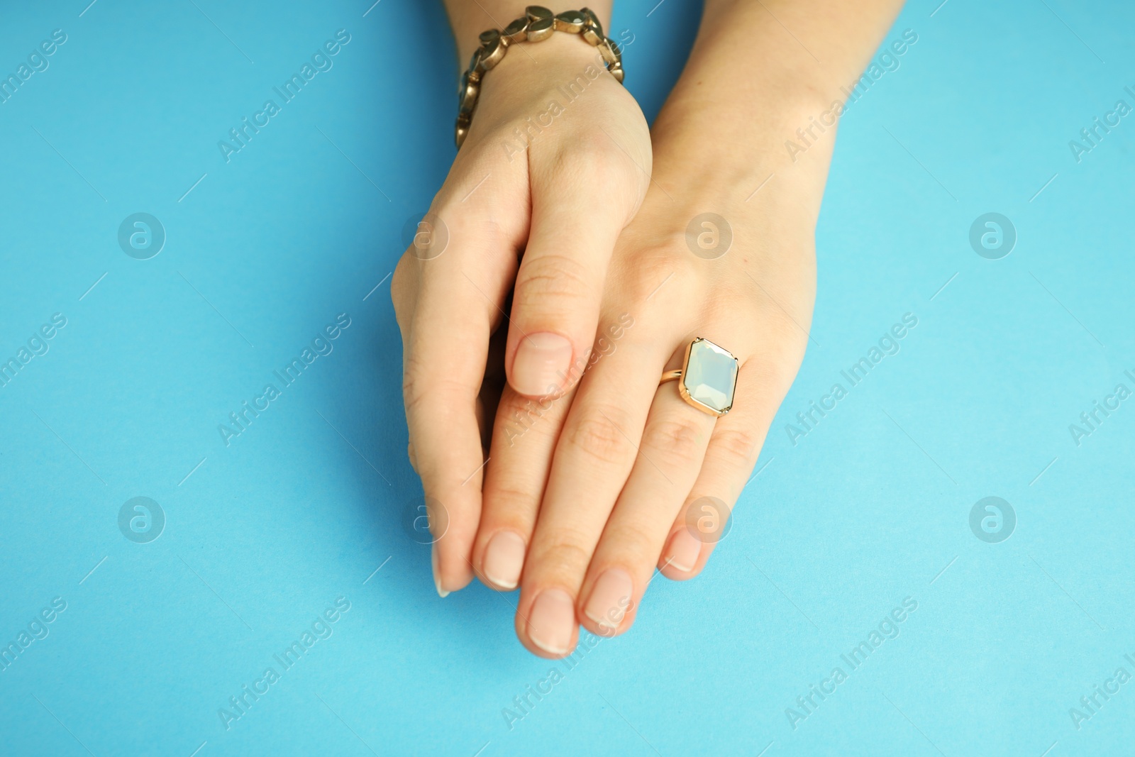 Photo of Beautiful bijouterie. Woman wearing stylish ring and bracelet on light blue background, closeup