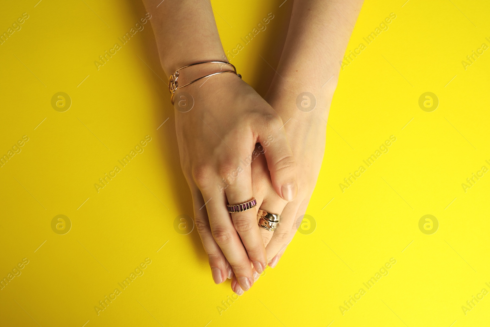 Photo of Beautiful bijouterie. Woman wearing different stylish rings and bracelet on yellow background, top view