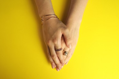 Photo of Beautiful bijouterie. Woman wearing different stylish rings and bracelet on yellow background, top view