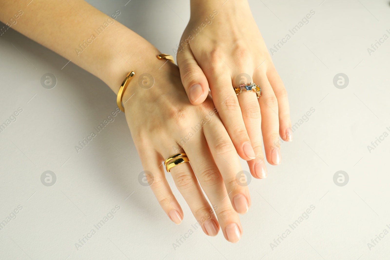 Photo of Beautiful bijouterie. Woman wearing stylish rings and bracelet on light grey background, closeup