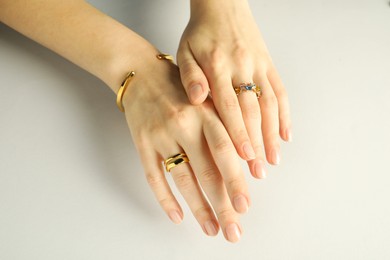 Photo of Beautiful bijouterie. Woman wearing stylish rings and bracelet on light grey background, closeup