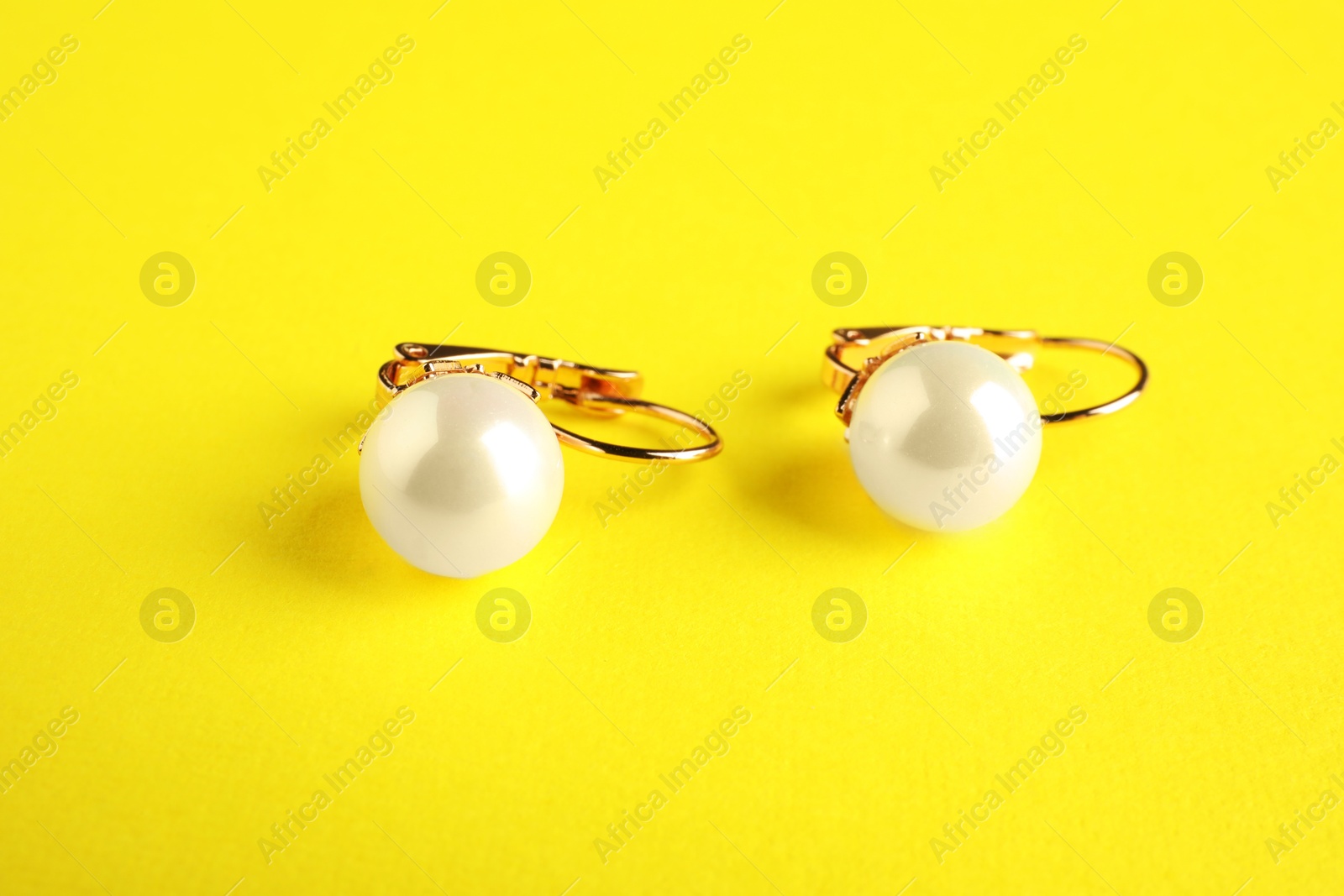 Photo of Beautiful bijouterie. Stylish earrings on yellow background, closeup