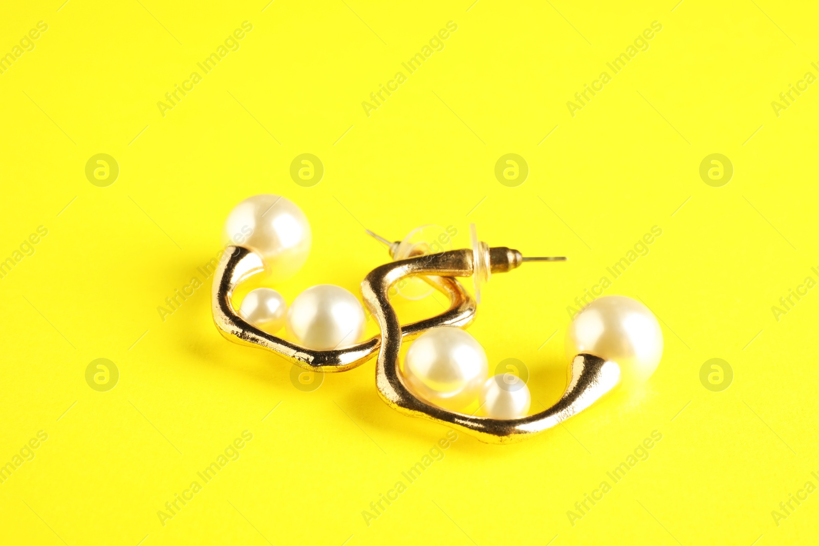 Photo of Beautiful bijouterie. Stylish earrings on yellow background, closeup