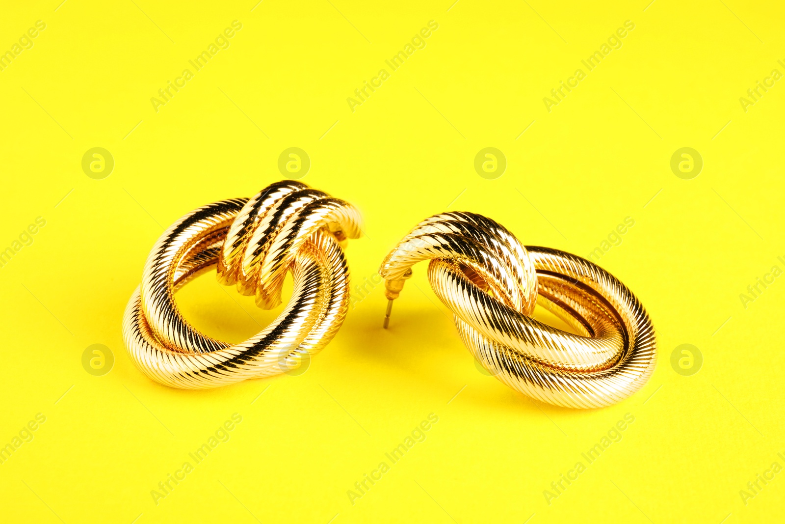 Photo of Beautiful bijouterie. Stylish earrings on yellow background, closeup