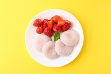 Photo of Delicious mochi and strawberries on yellow background, top view