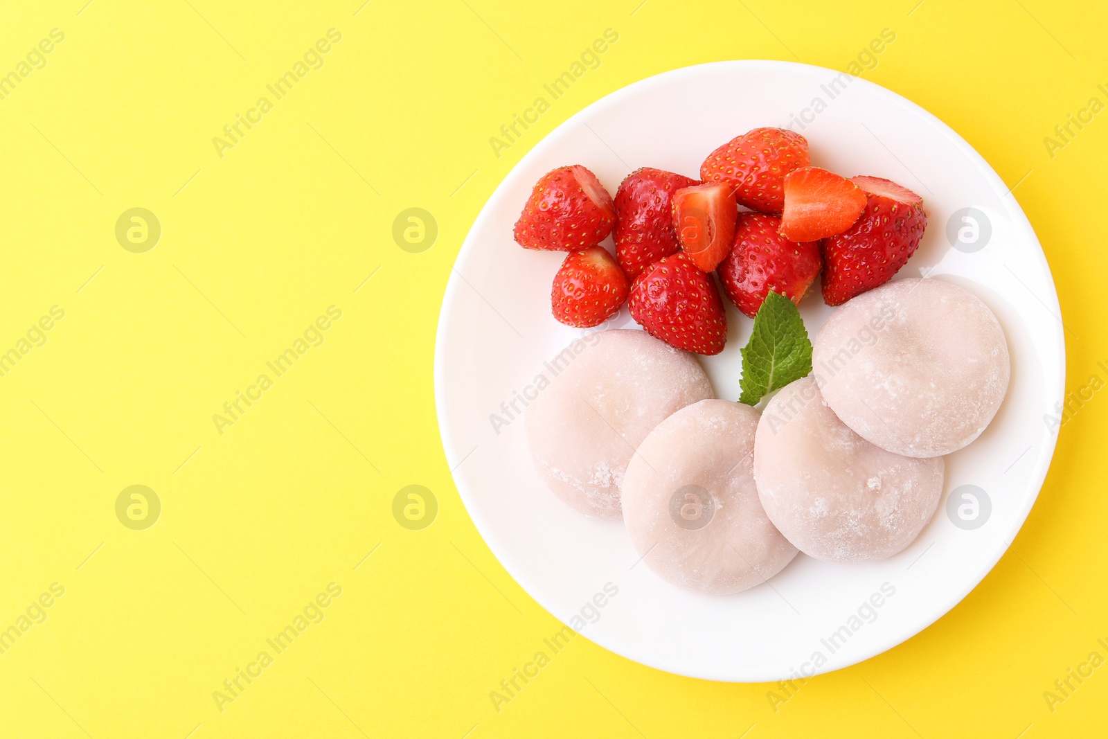 Photo of Delicious mochi and strawberries on yellow background, top view. Space for text