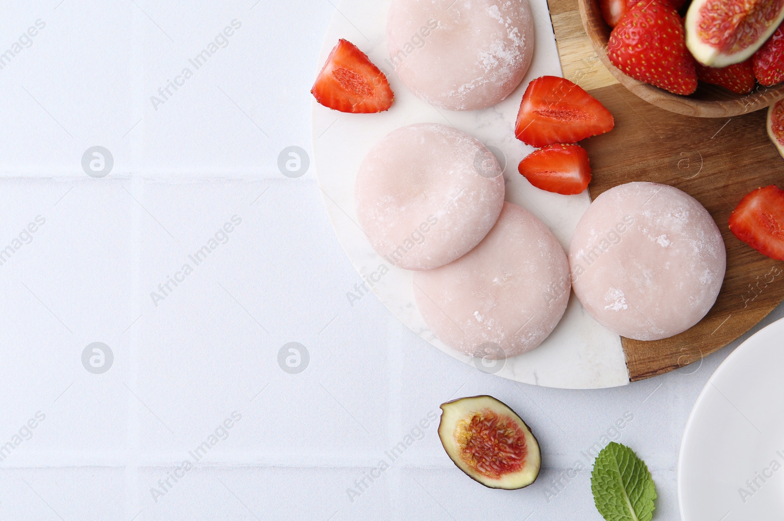 Photo of Delicious mochi, strawberries and figs on white tiled table, top view. Space for text