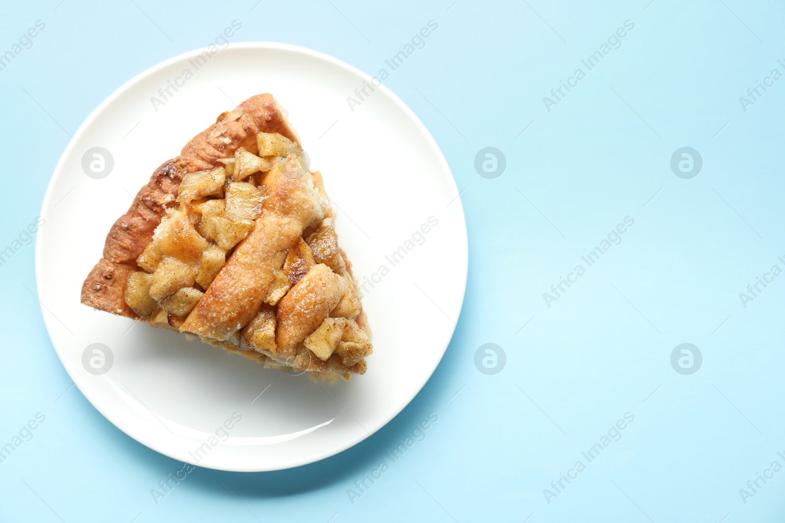 Photo of Slice of homemade apple pie on light blue background, top view. Space for text