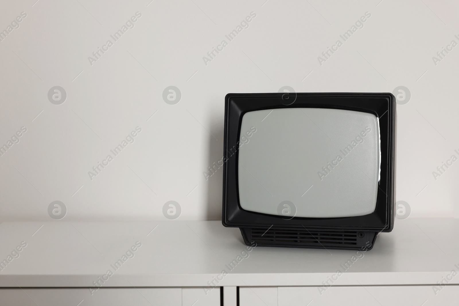 Photo of Retro tv set on chest of drawers against white wall. Space for text