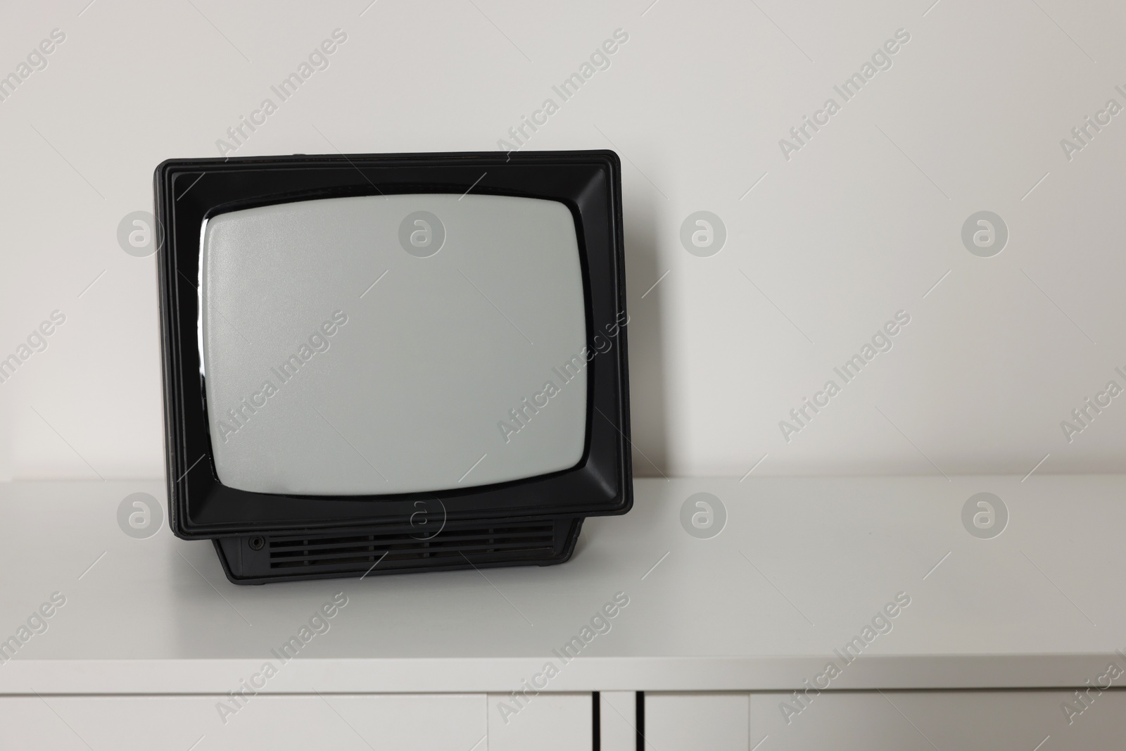 Photo of Retro tv set on chest of drawers against white wall. Space for text