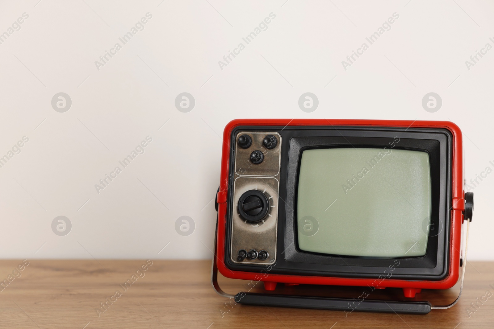 Photo of Retro tv set on wooden shelf against white wall. Space for text