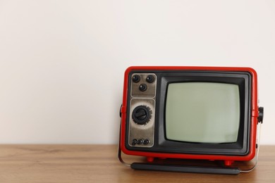 Photo of Retro tv set on wooden shelf against white wall. Space for text