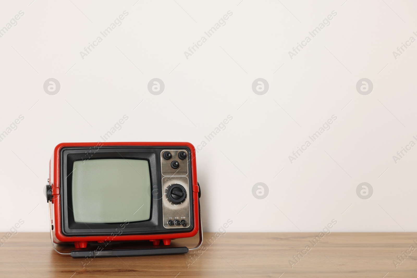 Photo of Retro tv set on wooden shelf against white wall. Space for text