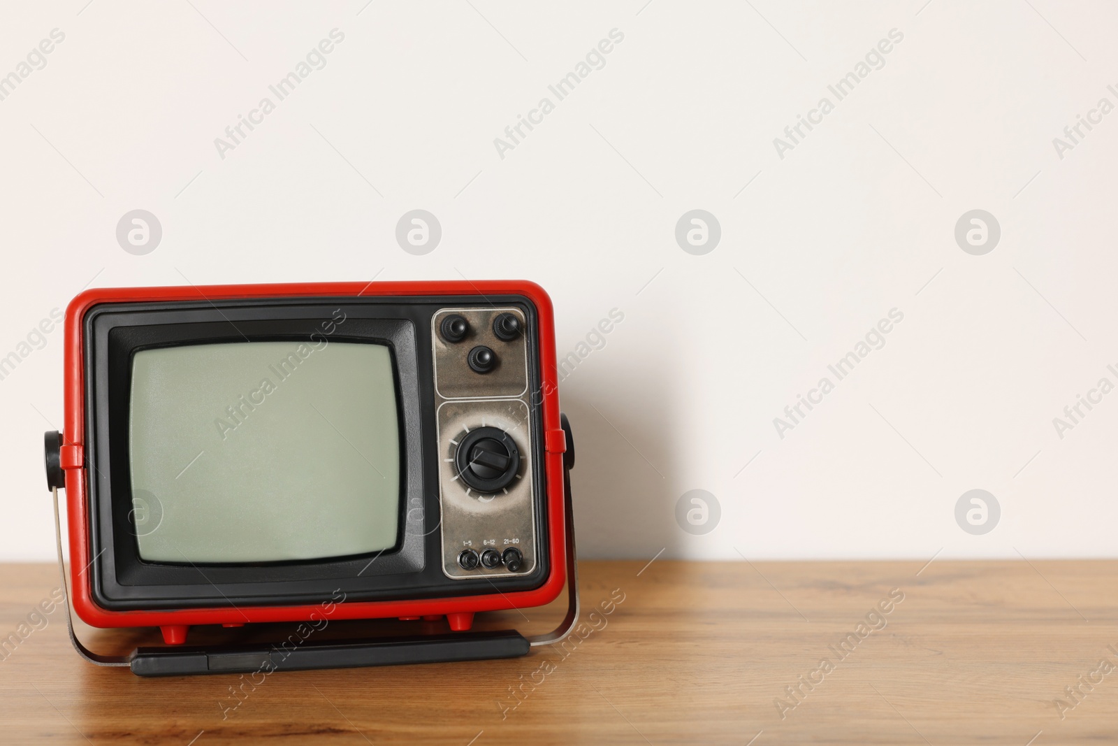 Photo of Retro tv set on wooden shelf against white wall. Space for text