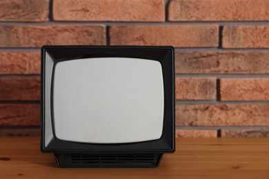 Photo of Retro tv set on wooden shelf against red brick wall. Space for text