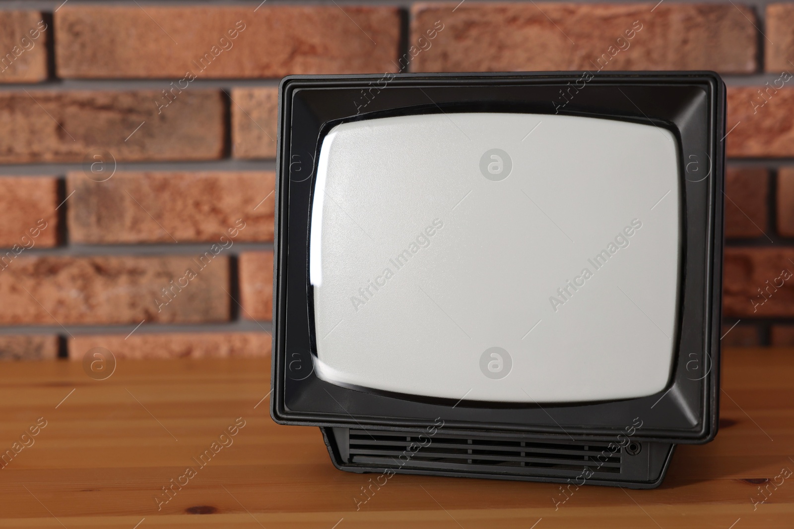 Photo of Retro tv set on wooden shelf against red brick wall. Space for text