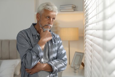 Photo of Lonely senior man looking out window indoors