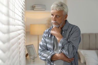 Photo of Lonely senior man looking out window indoors