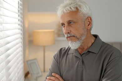 Photo of Lonely senior man looking out window indoors. Space for text