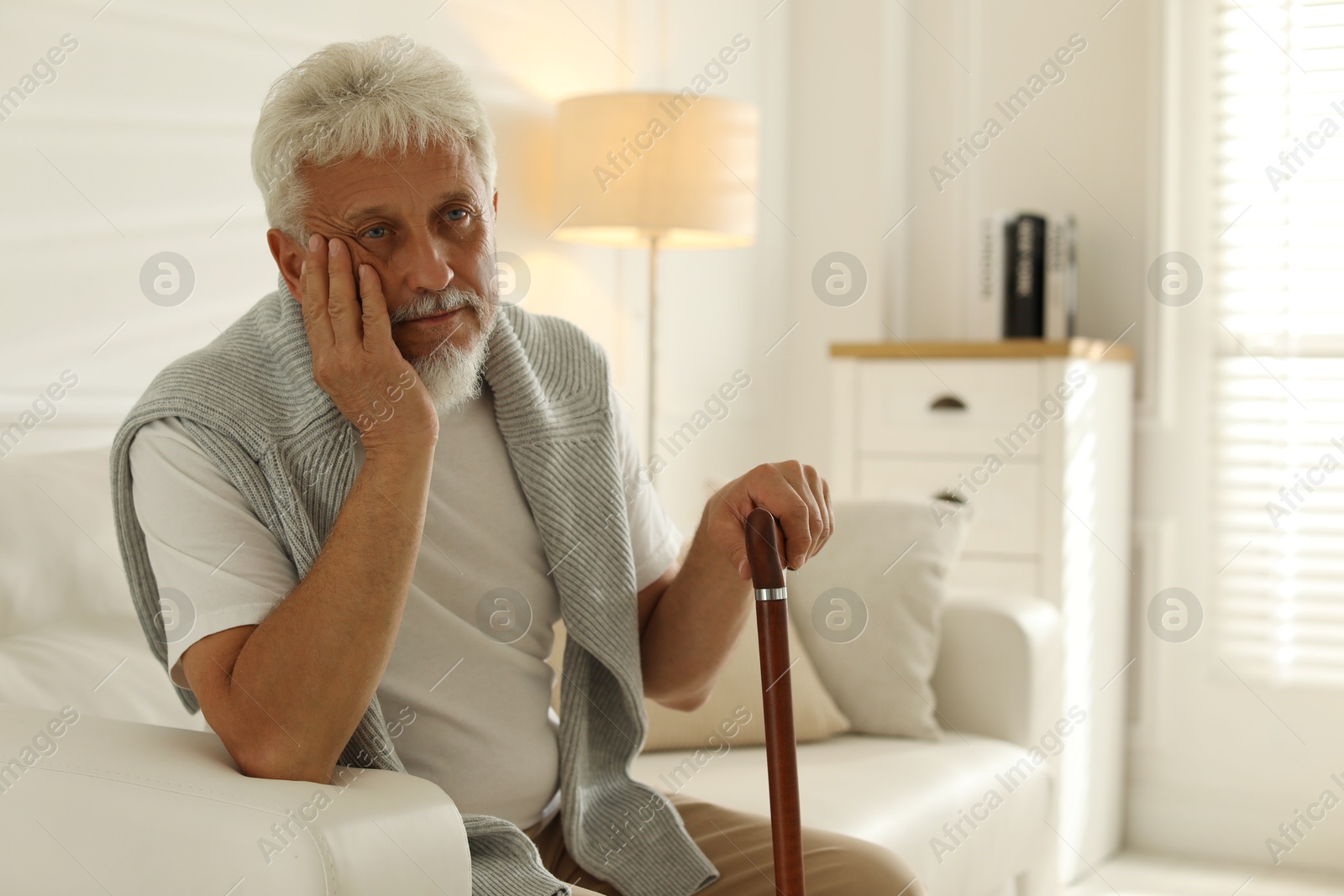 Photo of Lonely senior man with walking cane sitting on sofa at home. Space for text