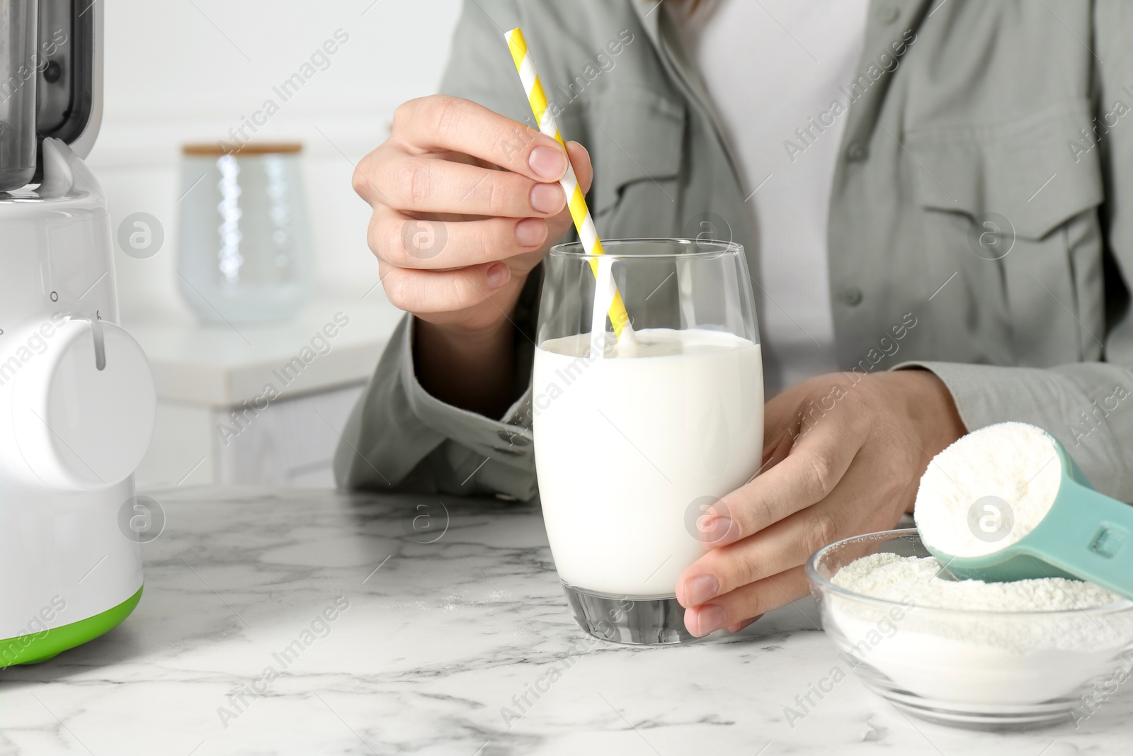 Photo of Woman with glass of protein cocktail at white marble table, closeup