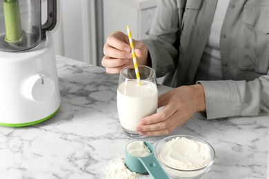 Photo of Woman with glass of protein cocktail at white marble table, closeup