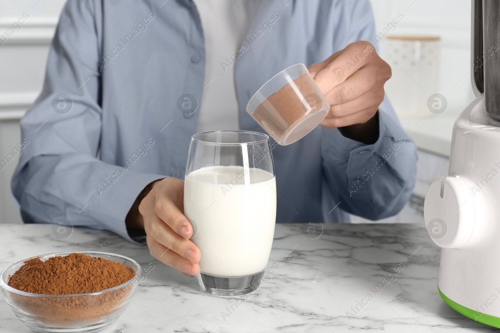 Photo of Making protein cocktail. Woman adding powder into glass with milk at white marble table, closeup