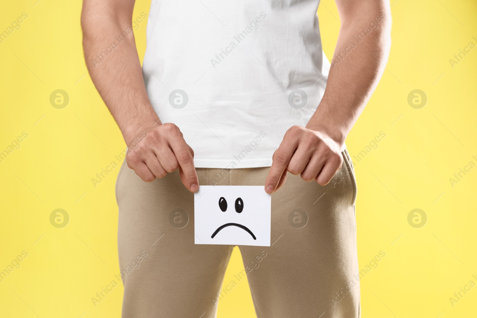 Photo of STD (sexually transmitted diseases). Man holding sticky note with drawn sad face on yellow background, closeup