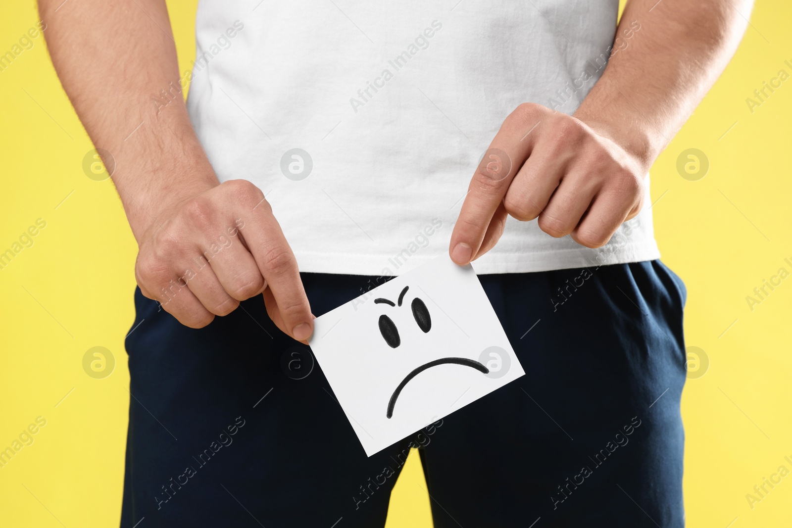 Photo of STD (sexually transmitted diseases). Man holding sticky note with drawn angry face on yellow background, closeup