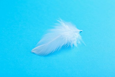 Photo of Beautiful fluffy feather on light blue background, closeup