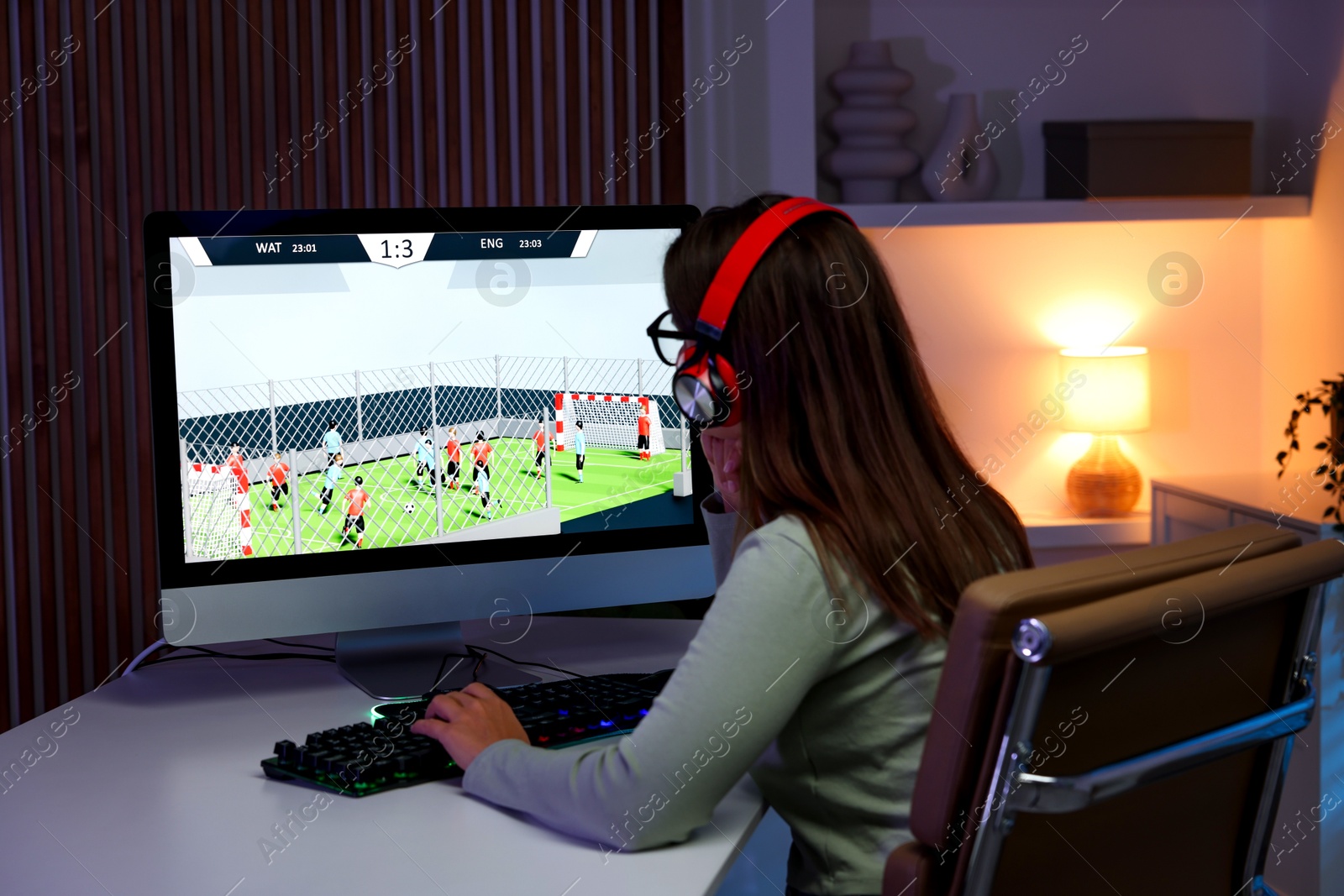 Photo of Woman in headphones playing video game with keyboard at table indoors