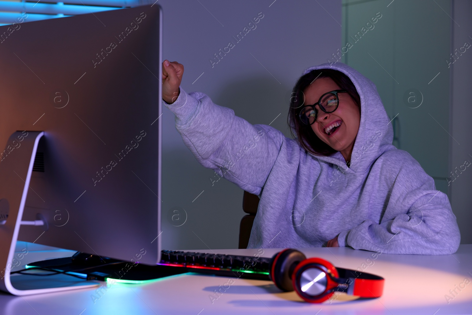 Photo of Happy woman playing video game at table with keyboard and monitor indoors