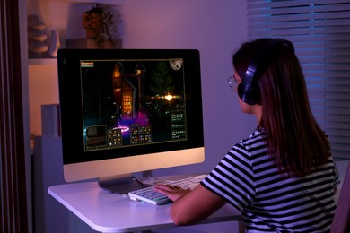 Photo of Woman playing video game with keyboard at table indoors, back view