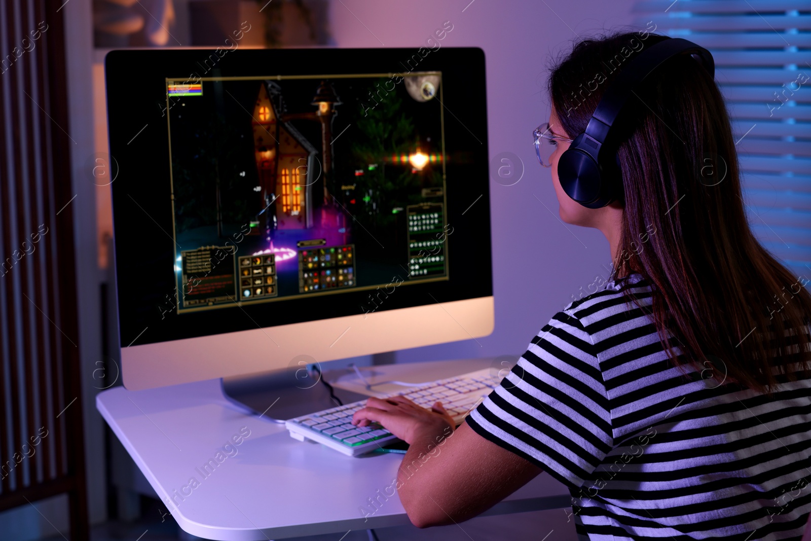 Photo of Woman playing video game with keyboard at table indoors, back view