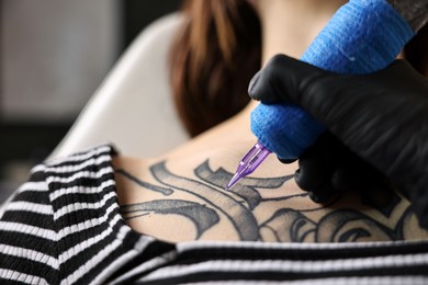 Photo of Professional artist tattooing woman with machine in salon, closeup