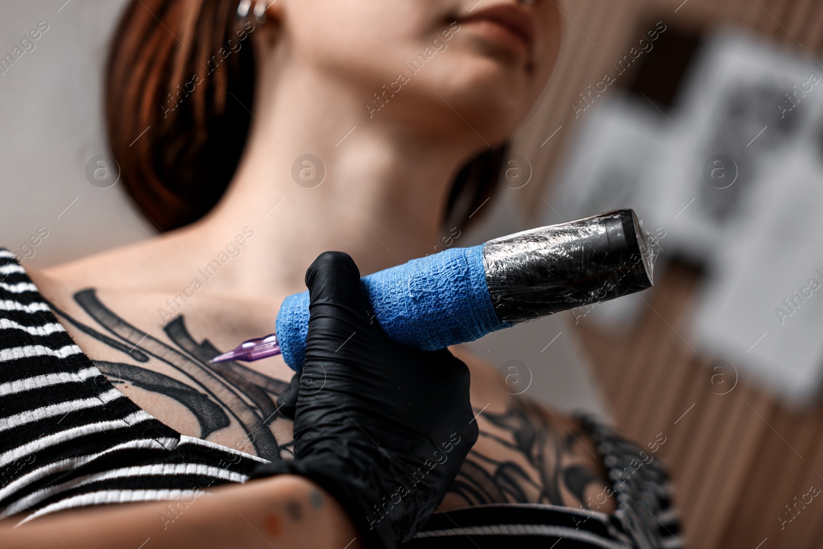 Photo of Professional artist tattooing woman with machine in salon, closeup