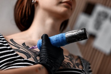 Photo of Professional artist tattooing woman with machine in salon, closeup