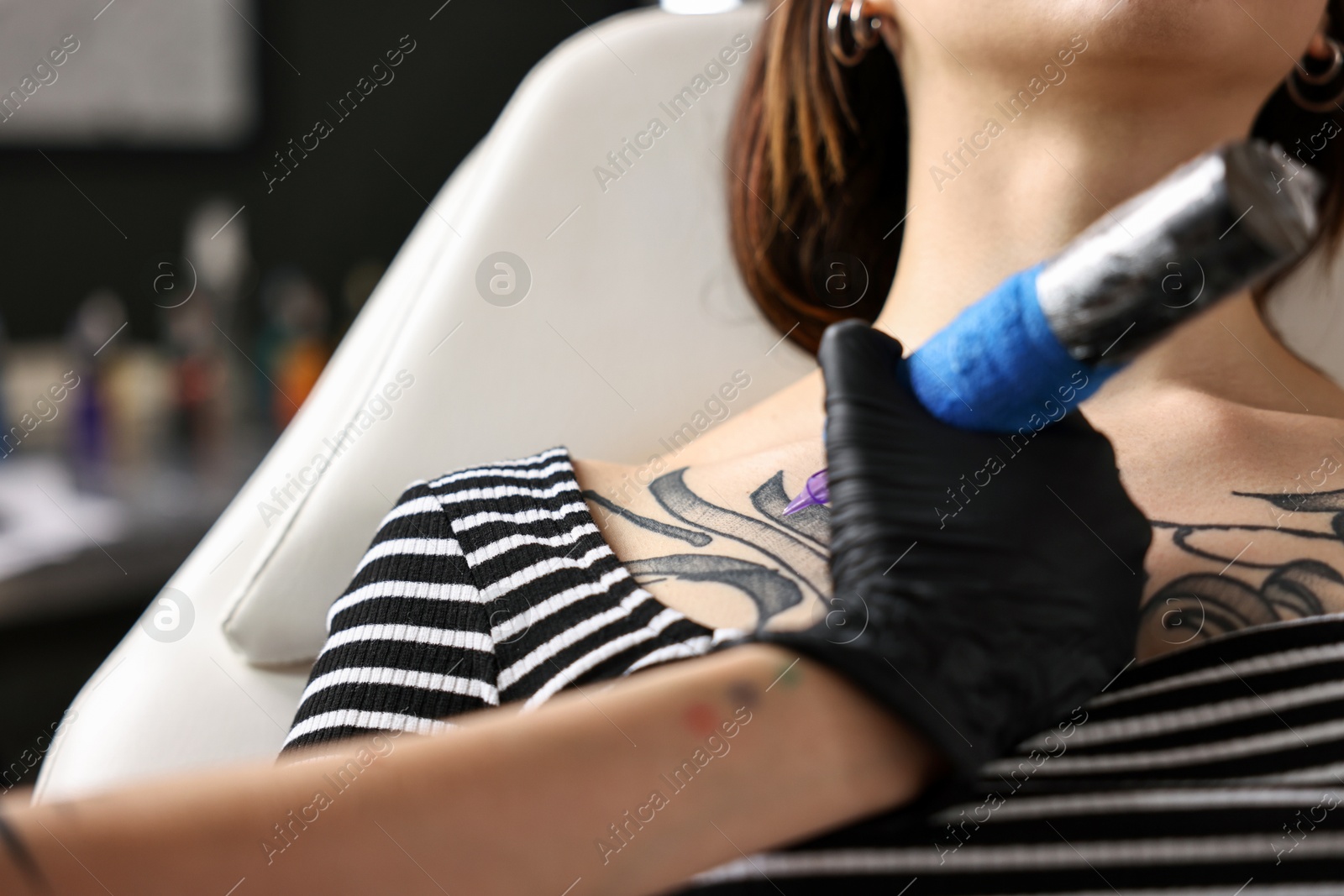 Photo of Professional artist tattooing woman with machine in salon, closeup