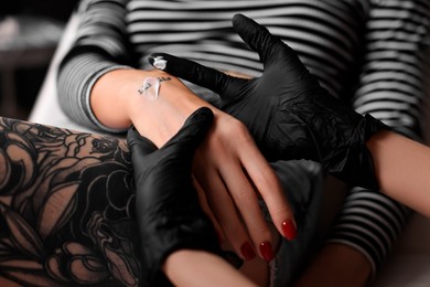 Photo of Professional artist in gloves applying cream onto woman's hand with fresh tattoo in salon, closeup