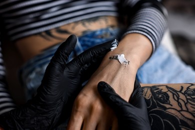 Photo of Professional artist in gloves applying cream onto woman's hand with fresh tattoo in salon, closeup