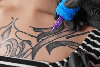 Photo of Professional artist tattooing woman with machine, closeup