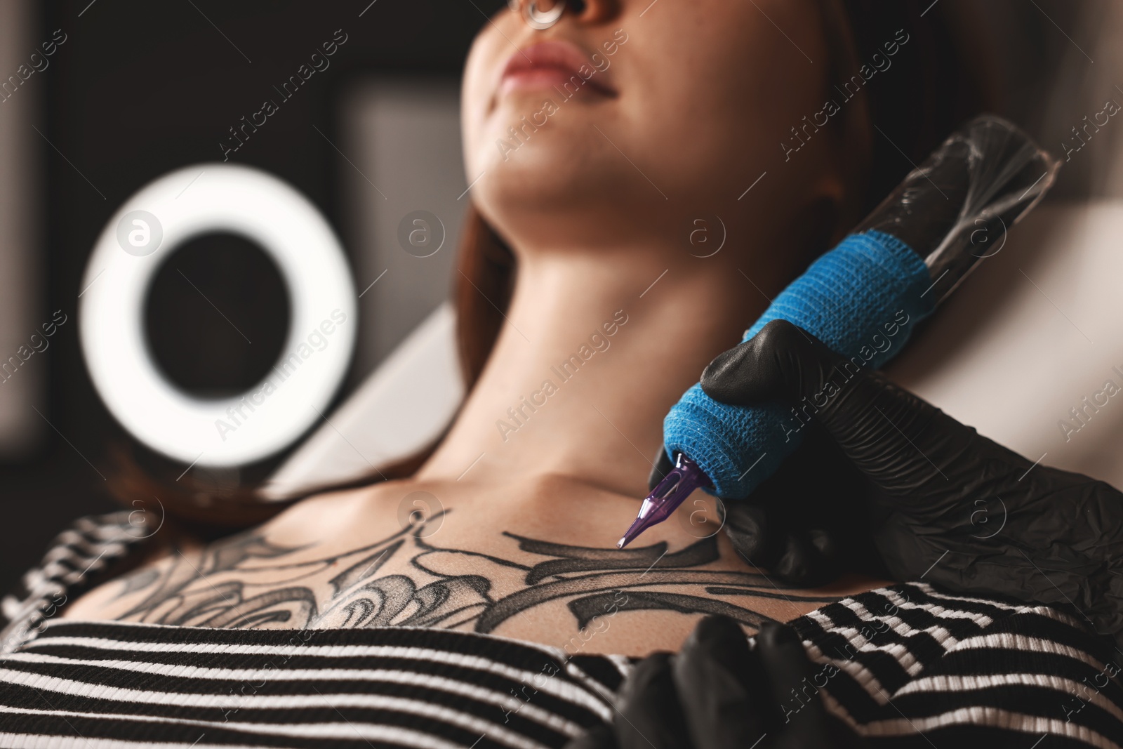 Photo of Professional artist tattooing woman with machine in salon, closeup