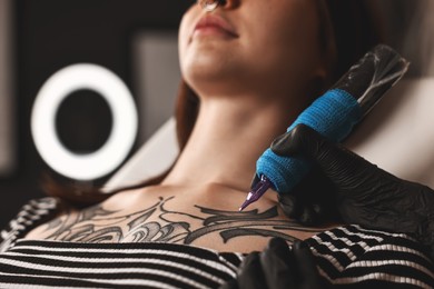 Photo of Professional artist tattooing woman with machine in salon, closeup