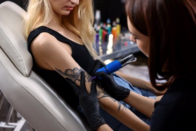 Photo of Professional artist tattooing woman's arm with machine in salon, closeup