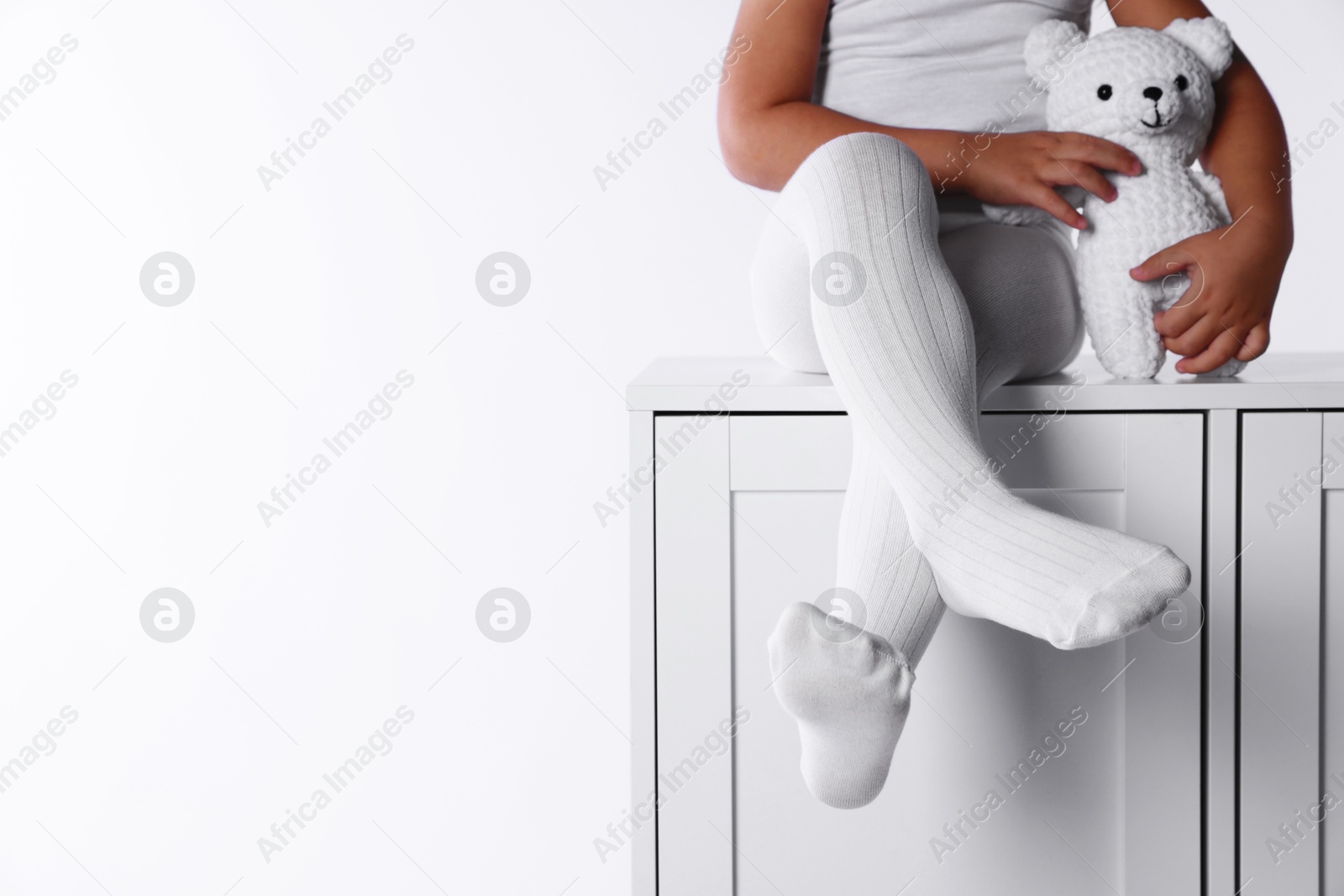 Photo of Child in tights sitting on cabinet against white background, closeup. Space for text