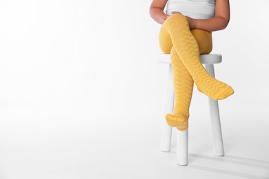 Photo of Child in bright tights sitting on stool against white background, closeup. Space for text