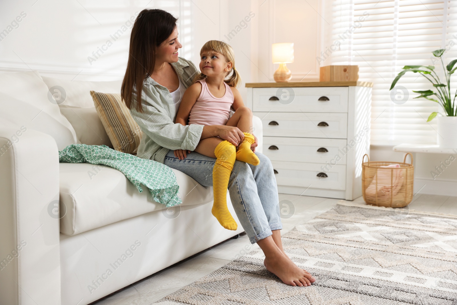 Photo of Mother helping her daughter to put tights on at home. Space for text